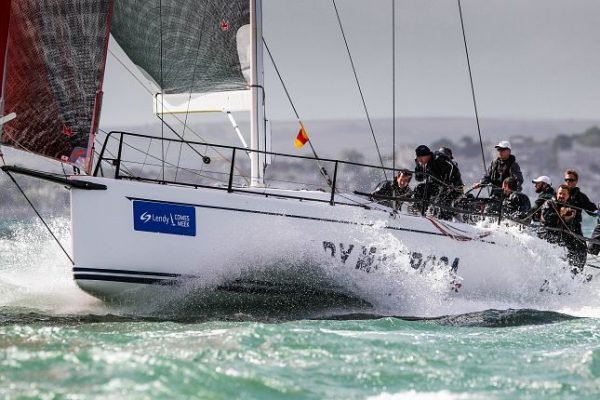 Dressed in wet weather gear, sailors on a white yacht navigate off the Isle of Wight