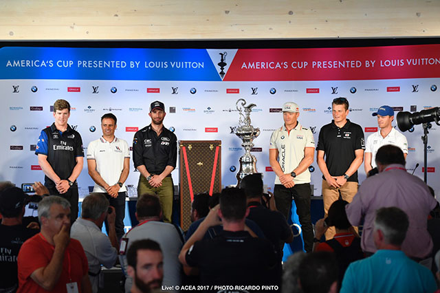 Six men dressed in polo shirts and baseball caps stand next to the America's Cup trophy