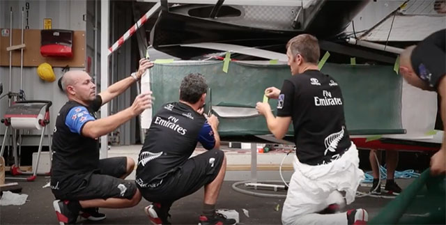 Three men make repairs to a catamaran ahead of the America's Cup
