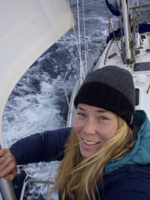 Golden Globe Race sailor wearing a black hat up the mast of her boat